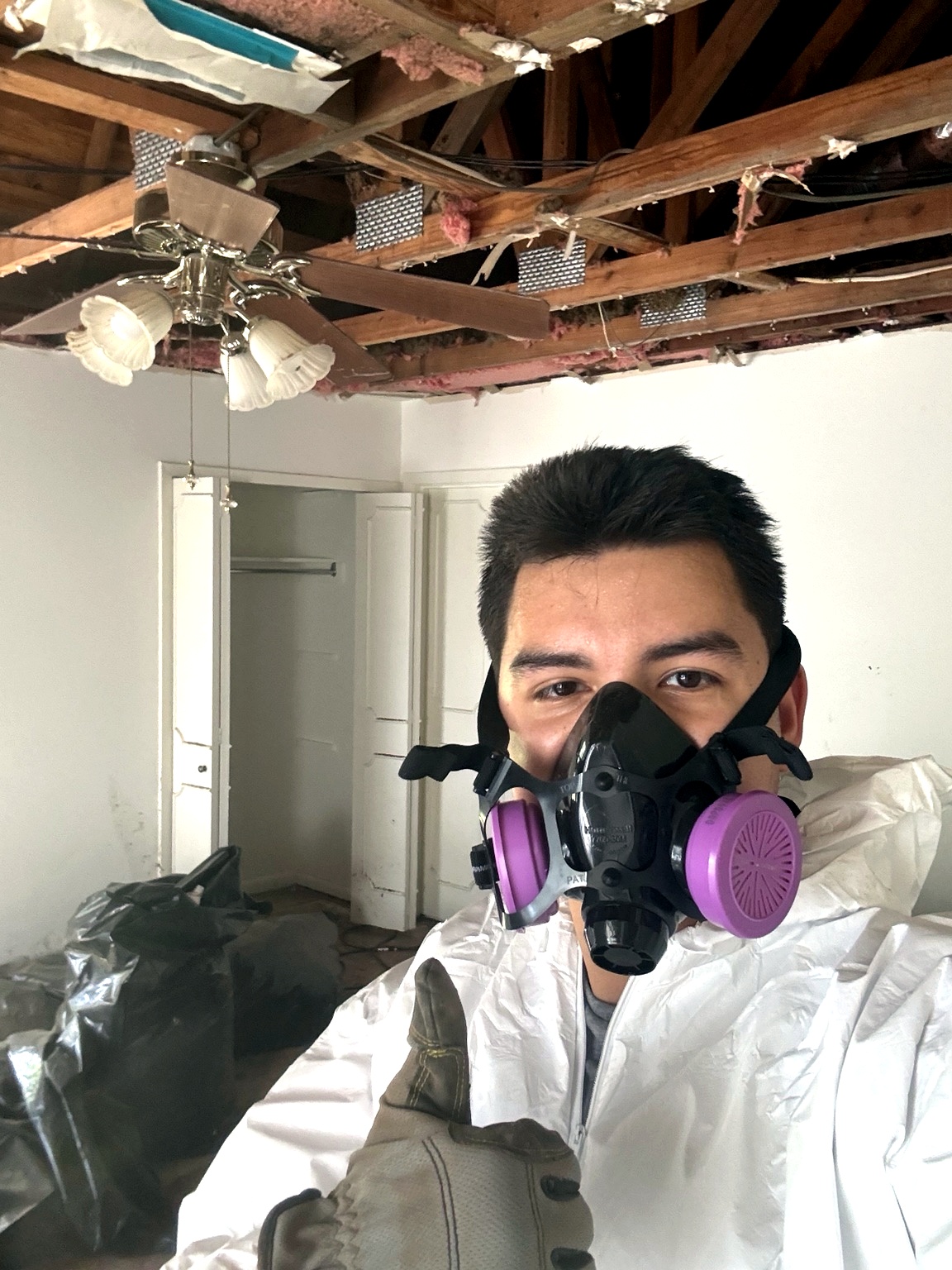 Emergency water damage restoration & mitigation in Leander, TX — IICRC certified technician in full PPE during ceiling demolition and water damage cleanup