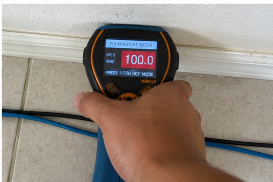 Emergency water damage cleanup & mitigation in Round Rock, TX — moisture meter reading 100% saturation on baseboard during water damage restoration